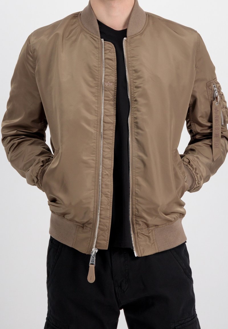 Giacca bomber marrone chiaro con zip frontale, polsini e orlo a costine, e tasche laterali. Materiale liscio e lucido con tasca con zip sulla manica.