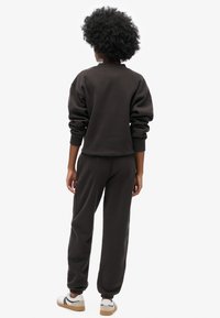 Sudadera gris oscuro con puños ajustados y pantalones deportivos a juego, con un ajuste relajado y textura suave, combinados con zapatillas blancas y detalles en negro.