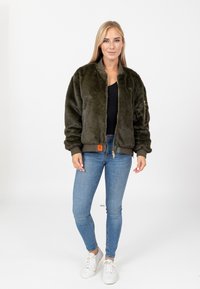 Faux-Fur-Bomberjacke in Olivgrün, mit Reißverschluss, gerippten Bündchen und Saum, seitlichen Taschen, weicher Textur und einem Etikett auf der Vorderseite.