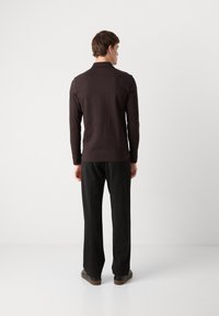 Mørkebrun langærmet polo t-shirt lavet af bomuld, parret med sorte bukser. T-shirten har en klassisk krave og en tætsiddende silhuet.