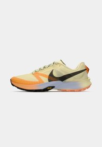 Skriešanas apavi ar dzeltenu acu audumu augšdaļā, oranžiem un melniem akcentiem, melnu Swoosh logotipu un teksturētu melnu zoli ar Vibram detalizāciju.