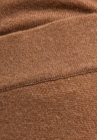 Brązowa dzianina o fakturowanym wykończeniu, z gładkim przeszyciem przejściowym. Kolor jest ciepły i jednolity na całej powierzchni.