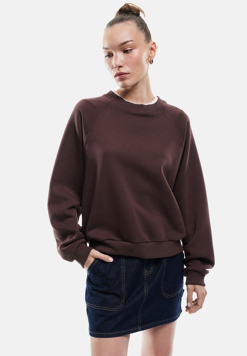 Bruine sweatshirt met ronde hals en raglanmouwen, gecombineerd met een donkerdenim minirok met voorzakken en een rechte zoom.