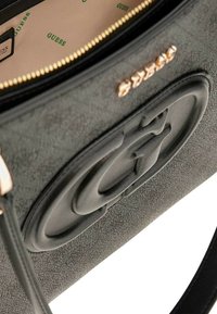 Borsa a mano in ecopelle nera con superficie testurizzata, caratterizzata da un grande logo in rilievo sul davanti, hardware color oro e un rivestimento interno beige.