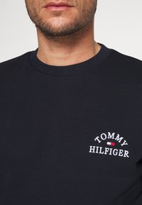 Sudadera de algodón navy con cuello redondo ribeteado, que presenta el logotipo "TOMMY HILFIGER" bordado en blanco y una raya de acento roja.