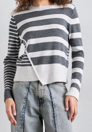 Harmaa ja valkoinen raidallinen neule, jossa on ainutlaatuinen epäsymmetrinen helma, ribbireunat ja pehmeä, teksturoitu kangas. Yhdistetty kuluneisiin farkkuihin.