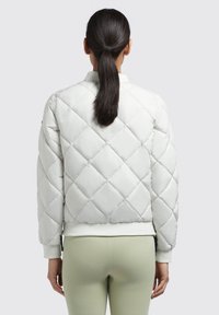White quilted puffer jacket with a fitted design, ribbed cuffs and hem, and a smooth texture, shown from the back with a ponytail hairstyle.