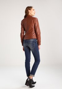 Brun læderjakke med quiltede skuldre, slim fit, parret med mørkeblå jeans og sorte ankelstøvler. Bagview viser en skræddersyet silhuet.