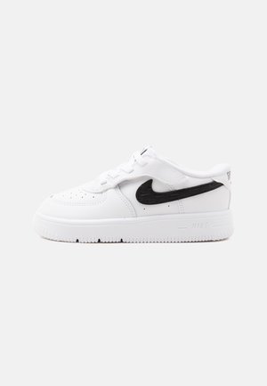 Valge Nike toss musta Swooshi logoga, paeltega ja paksu tallaga, helel taustal, külgvaates.