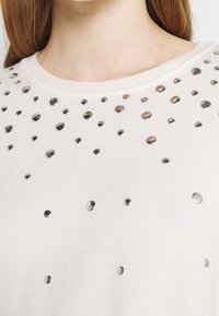 Helles rosa Sweatshirt mit rundem Ausschnitt und mit silbernen Verzierungen, die in einem verstreuten Muster über die Vorderseite angeordnet sind.