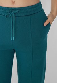 Türkise Jogginghose mit Kordelzugbund, Seitentaschen und einem glatten, strukturierten Stofffinish. Designed für Komfort und Freizeitkleidung.