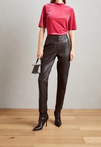 Haut rouge en velours à manches courtes associé à un pantalon en cuir noir taille haute et des bottes à talons aiguilles noires à bout pointu ; comprend un petit sac à main.