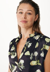Mørk floral bluse med korte ærmer, V-hals og et mønster af grønne blade og hvide blomster på en sort baggrund.