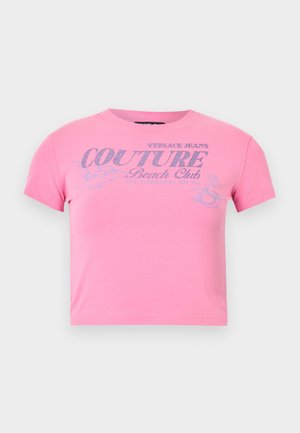 Ροζ κοντομάνικο crop top με ασημί γκλίτερ κείμενο "Versace Jeans Couture Beach Club" και ένα μικρό γραφικό μιας γυναίκας που κάνει σέρφινγκ.