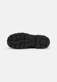 Suela de zapato de goma negra con patrones de relieve profundos, que incluyen un diseño en zigzag y un logo redondo cerca del talón. Superficie duradera y texturizada.