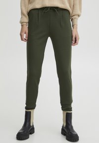 Olijfgroene tapered joggers met een voorplooien en een verstelbare tailleband, gecombineerd met zwarte enkellaarsjes met een beige accent.