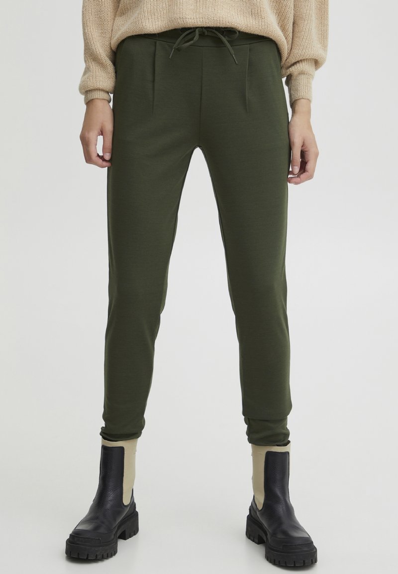 Olijfgroene tapered joggers met een voorplooien en een verstelbare tailleband, gecombineerd met zwarte enkellaarsjes met een beige accent.