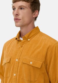Senfgelbes Cordhemd mit Button-Down-Kragen, zwei Brusttaschen und einem strukturierten, gerippten Stoff.
