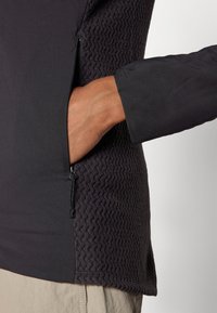 Zwarte fleece-gevoerde jas met een textuurpaneel, zijzak met rits en een gladde stof. Beschikt over omgeslagen mouwen en een relaxed fit ontwerp.
