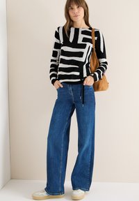 Pasiasty czarno-biały sweter, luźne niebieskie dżinsy, kremowe sneakersy z teksturowaną podeszwą, brązowa zamszowa torba na ramię.