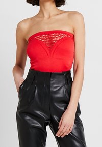 Rode strapless top met een geperforeerde mesh overlay, gecombineerd met hoge zwarte faux leren broeken met geplooide details.