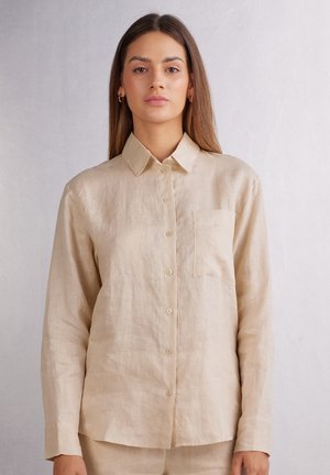 Beige Leinenhemd mit Knopfverschluss, langen Ärmeln, spitzem Kragen, einer Brusttasche und feiner Textur. Weicher, leichter Stoff.