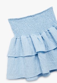 Falda de tierna azul claro hecha de tela texturizada. Cuenta con una cintura elástica fruncida y dos capas con volantes en el bajo.