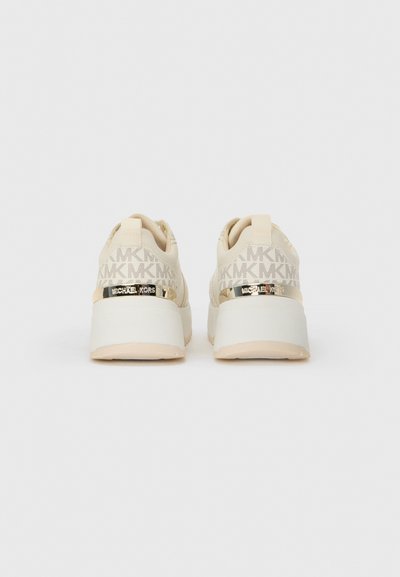 Zapatillas beige con parte superior de tela texturizada que presenta el logo repetido de MK, detalles en tono dorado y una suela blanca gruesa.
