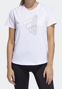 Hvid atletisk T-shirt med korte ærmer, der har et sort Adidas-logo i et geometrisk design på forsiden. Glat stoffets tekstur.