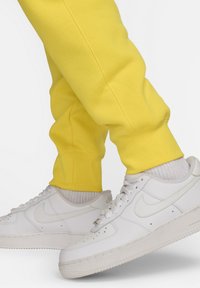 Pantalones de chándal amarillos hechos de una mezcla de algodón, con un ajuste relajado y puños elásticos, combinados con zapatillas Nike de cuero blanco.