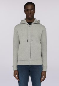 Grå zip-up huvtröja med huva, med dragsnören och en framficka. Bärs över en svart tröja, tillsammans med blå jeans. Slät textur.