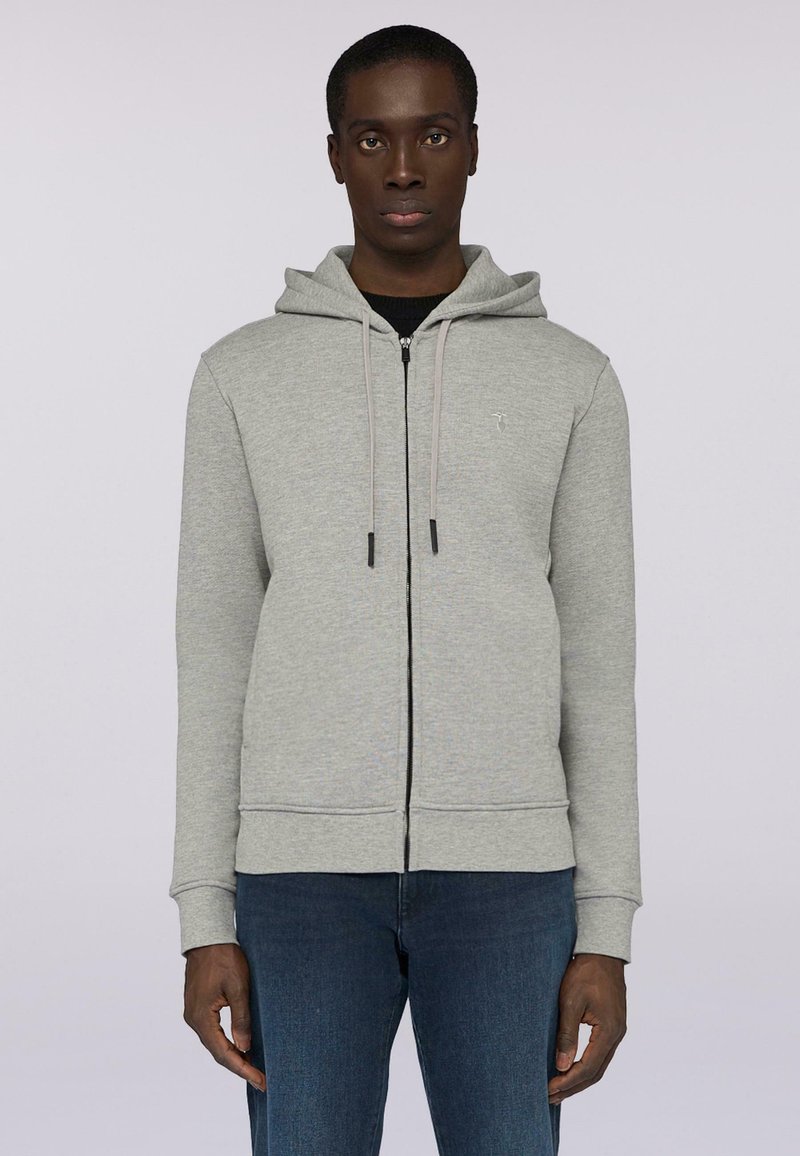 Grå zip-up huvtröja med huva, med dragsnören och en framficka. Bärs över en svart tröja, tillsammans med blå jeans. Slät textur.