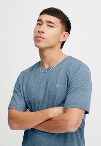 Niebieska koszulka z krótkim rękawem wykonana z fakturowanej tkaniny, z małym logo na piersi. Prosty, luźny krój z okrągłym dekoltem.