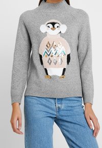 Grå stickad tröja med hög krage, med en pingvindesign i rosa och svart, samt färgglada geometriska mönster och glänsande detaljer.