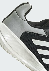 Scarpa da ginnastica nera e grigia con tomaia in mesh testurizzato, accenti sintetici lisci e una suola in gomma bianca con motivi di scolpitura.