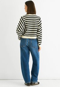 Black and white striped knit sweater with a cropped design, paired with loose blue jeans. The sweater features ribbed cuffs and hem.