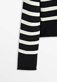 Manche en tissu tricoté noir avec des rayures blanches horizontales espacées de manière régulière sur un fond clair uni.