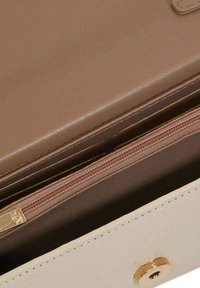 Lichtbeige handtas met een gladde textuur, voorzien van een gouden rits en ronde hardware-accenten. De binnenvoering is van zacht bruin stof.