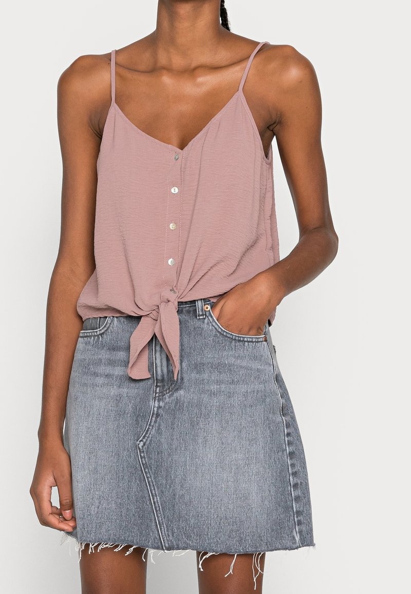 Haut rose sans manches avec un détail noué à l'avant, associé à une jupe en denim gris présentant un ourlet effiloché et un design classique à cinq poches.