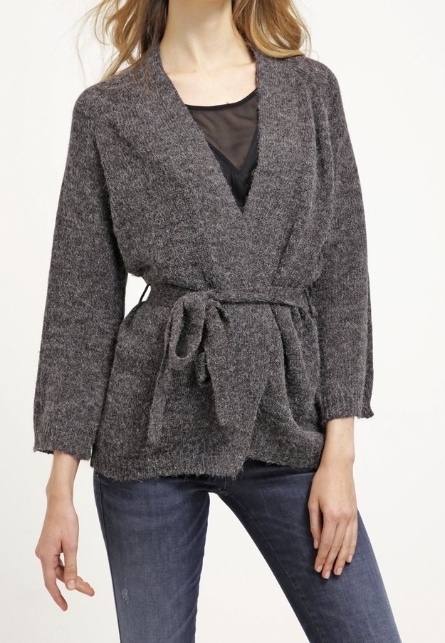 Cardigan gris en tricot avec un design enveloppant, ceinturé à la taille. Il comporte des manches longues et un tissu texturé. Porté par-dessus un haut noir.