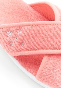 Sandalo slide in tessuto rosa corallo con una texture morbida, cinturini incrociati e ricamo di stelle argento sulla parte superiore. Suola bianca visibile sotto.