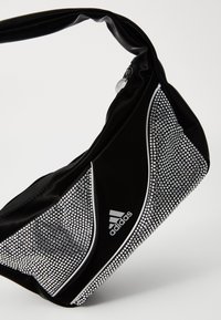 Crna torba sa sjajnom, teksturiranom površinom, ukrašena srebrnim rhinestonesom i opremljena zakrivljenim remenom i Adidas logotipom.