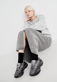 Gray hooded sweatshirt, gray denim skirt with side slits, black socks, and gray sneakers with textured surfaces and laces.