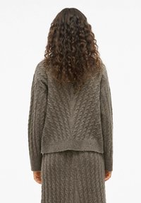 Maglione a maglia grossa e gonna coordinata in un morbido colore taupe. Presenta un motivo a trecce e orlo a coste, con maniche lunghe e vestibilità rilassata.