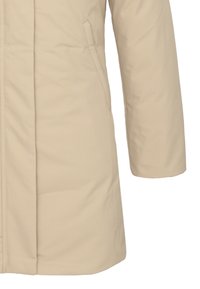 Cappotto isolato beige con una texture liscia, caratterizzato da cuciture diagonali, tasche laterali e un orlo dritto. Maniche lunghe con vestibilità ampia.