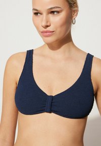 Granatowy biustonosz bikini z teksturowanej tkaniny, szerokimi ramiączkami i centralnym węzłem, z gładkim brzegiem i trójkątnym kształtem.