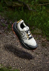 Lichte trailrunning schoen met een mesh bovenkant in crème, een gevoerde zwarte zool en oranje accenten, voorzien van een veilig vetersysteem.