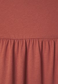 Tissu couleur rouille avec une texture lisse, surmonté d'un ourlet froncé, créant un élément de design doux et fluide en bas.