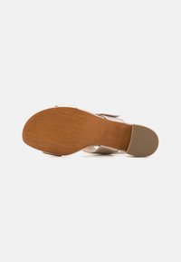 Sandal with a light tan leather upper and wooden sole. Features a textured bottom with a ridged pattern for grip.