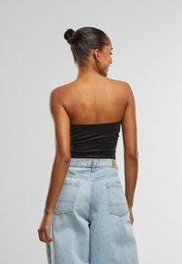 Top negru fără bretele, asortat cu blugi deschis la culoare, cu talie înaltă. Materialul pare neted, iar blugii au o croială lejeră, cu buzunare în spate.